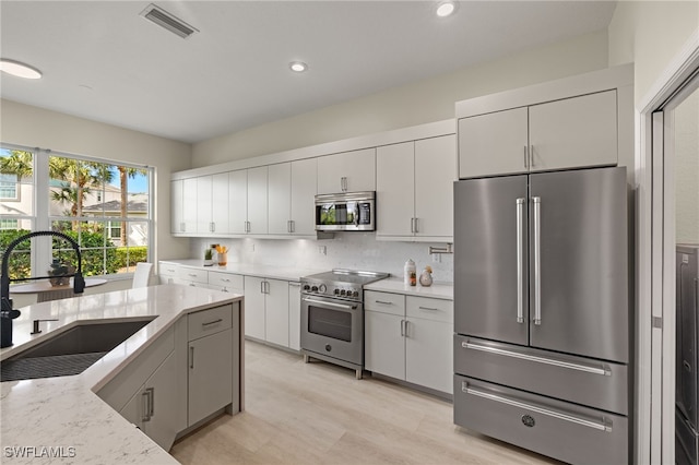 kitchen with high end appliances, tasteful backsplash, sink, and light stone counters