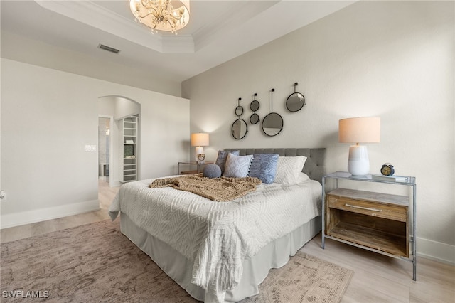 bedroom with an inviting chandelier, ornamental molding, a tray ceiling, and light wood-type flooring