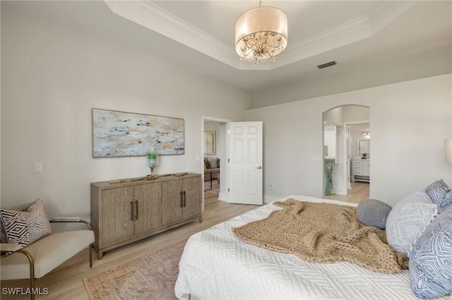 bedroom with an inviting chandelier, a tray ceiling, ornamental molding, and light wood-type flooring