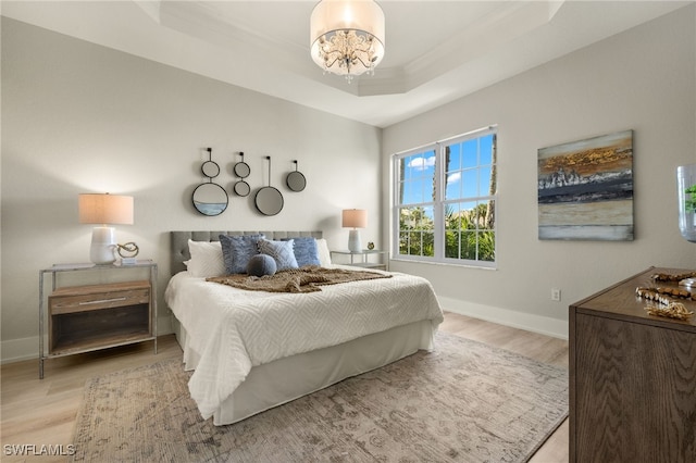 bedroom featuring a raised ceiling, a notable chandelier, and light hardwood / wood-style floors