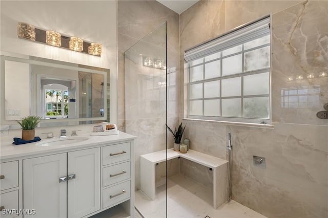 bathroom with a tile shower, vanity, and tile walls