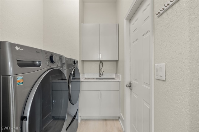 washroom featuring cabinets, sink, washing machine and dryer, and light hardwood / wood-style flooring