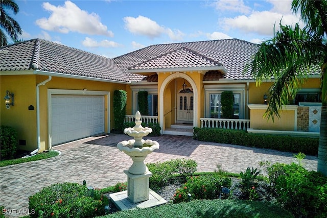 mediterranean / spanish house featuring decorative driveway, french doors, a garage, and stucco siding