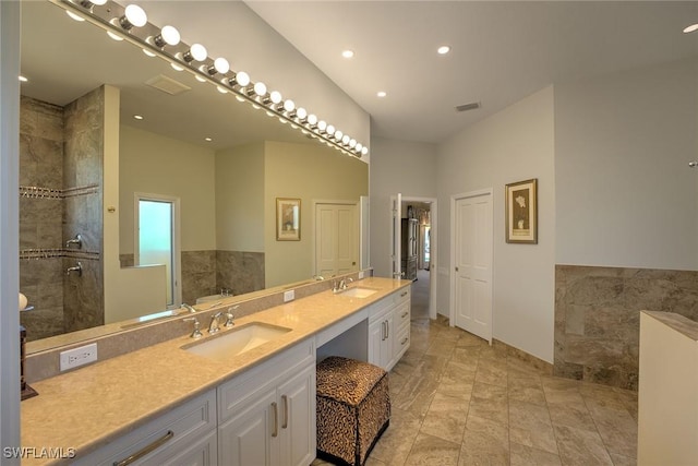 bathroom with a sink, visible vents, double vanity, and a tile shower