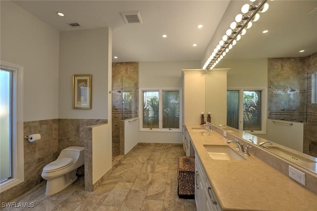 full bathroom with visible vents, toilet, a tile shower, tile walls, and a sink