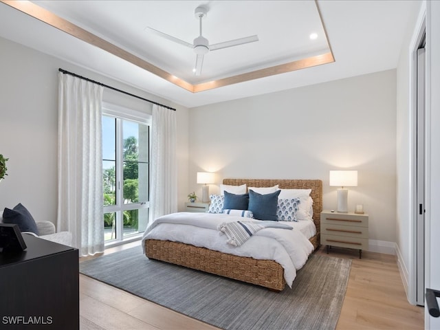 bedroom with ceiling fan, a tray ceiling, and light hardwood / wood-style flooring