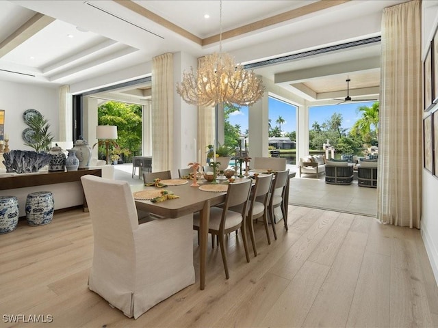 dining space featuring a tray ceiling, ceiling fan with notable chandelier, and light wood-type flooring