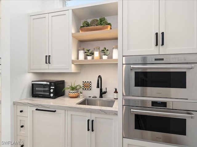 kitchen with sink, white cabinetry, tasteful backsplash, double oven, and light stone countertops