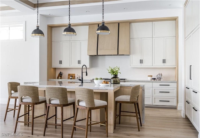 kitchen with decorative light fixtures, an island with sink, and white cabinets