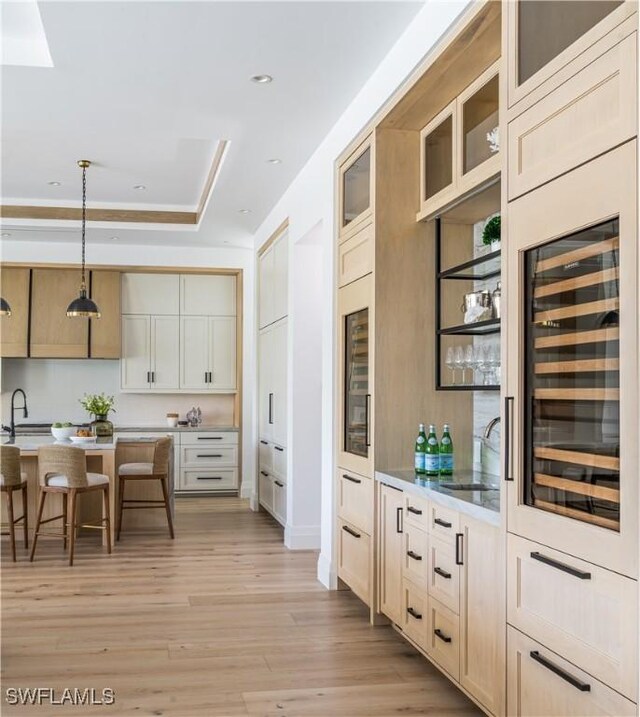 kitchen featuring sink, a breakfast bar area, wine cooler, light hardwood / wood-style floors, and decorative light fixtures