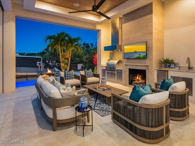 patio terrace at dusk featuring an outdoor living space with a fireplace, sink, exterior kitchen, grilling area, and ceiling fan