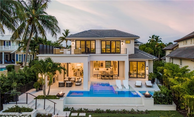 back house at dusk featuring a balcony, an outdoor living space with a fire pit, and a patio area