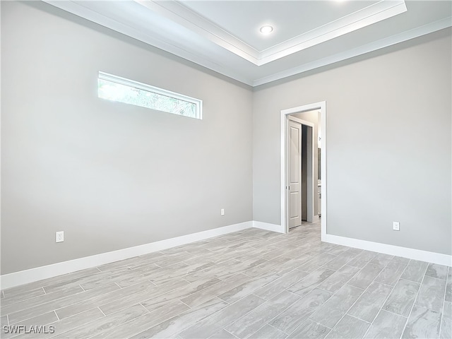 empty room with light wood-type flooring, crown molding, and a raised ceiling