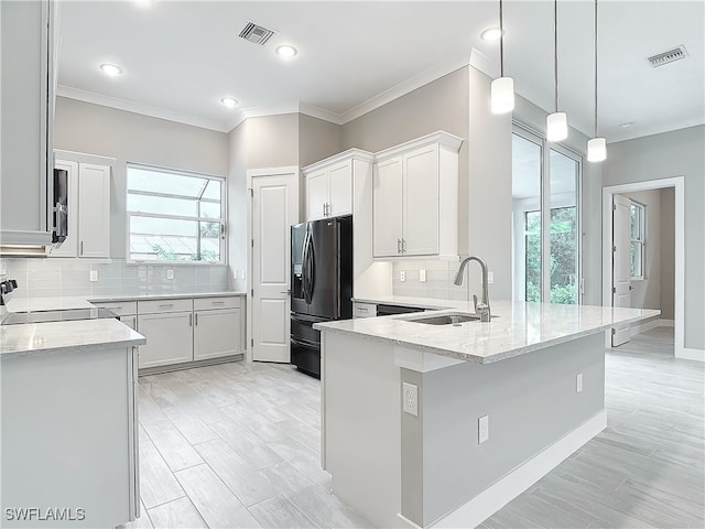 kitchen with white cabinets, sink, black fridge, and plenty of natural light