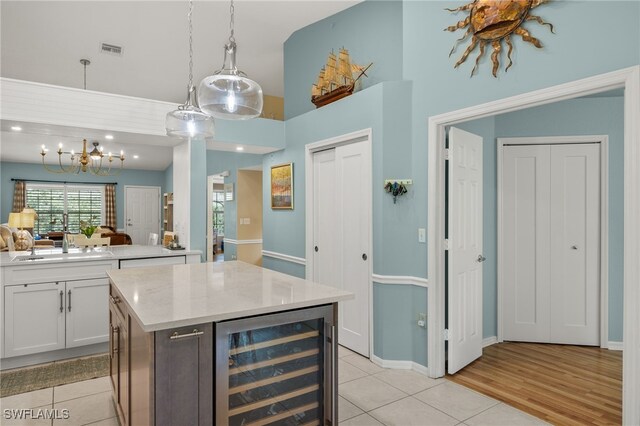 kitchen with light hardwood / wood-style flooring, beverage cooler, a center island, light stone counters, and white cabinets