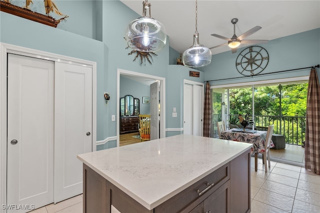 kitchen with a kitchen island, ceiling fan, light stone countertops, and high vaulted ceiling