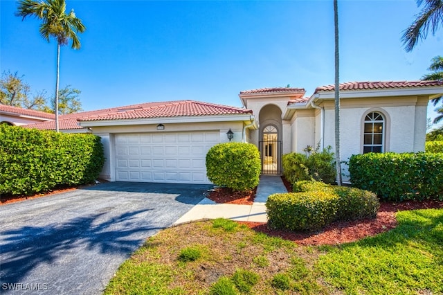 mediterranean / spanish-style house featuring a garage, a tile roof, stucco siding, and aphalt driveway