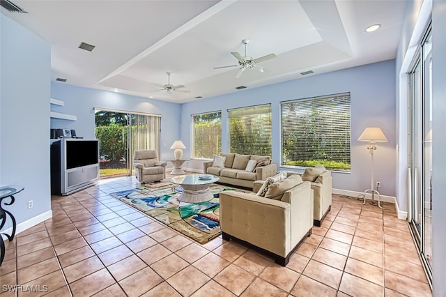 living room featuring ceiling fan, a raised ceiling, and light tile patterned flooring