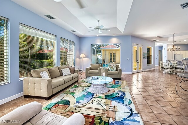 living room with ceiling fan with notable chandelier, light tile patterned floors, plenty of natural light, and a raised ceiling