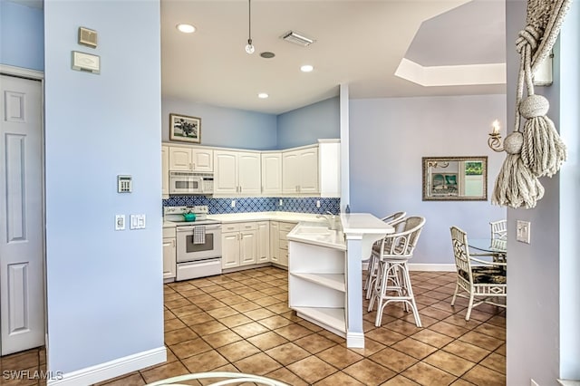 kitchen with white appliances, light tile patterned floors, a breakfast bar, kitchen peninsula, and white cabinetry