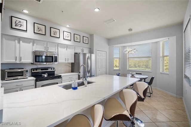 kitchen featuring stainless steel appliances, pendant lighting, light tile patterned floors, sink, and white cabinetry