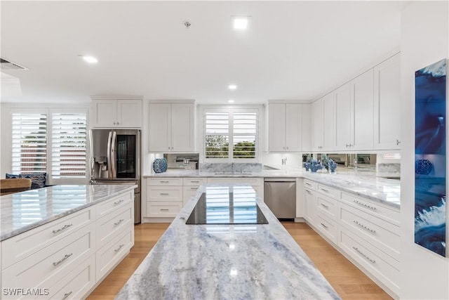 kitchen with light stone countertops, white cabinets, light wood-type flooring, and appliances with stainless steel finishes