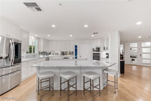 kitchen with light stone countertops, light wood-type flooring, stainless steel appliances, a spacious island, and white cabinetry