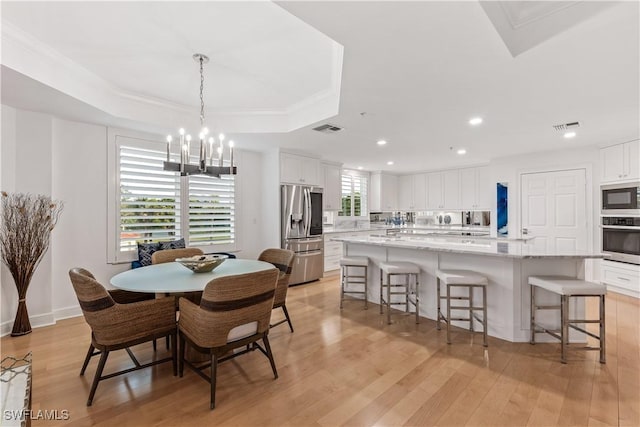 dining area featuring a tray ceiling, a chandelier, light hardwood / wood-style floors, and ornamental molding