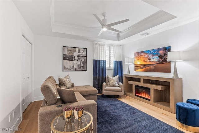 living room with a tray ceiling, ceiling fan, hardwood / wood-style floors, and ornamental molding