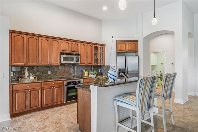 kitchen with decorative light fixtures, appliances with stainless steel finishes, dark stone counters, washing machine and dryer, and backsplash