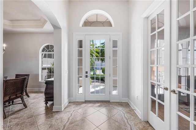 doorway featuring french doors, ornamental molding, a tray ceiling, and light tile patterned flooring