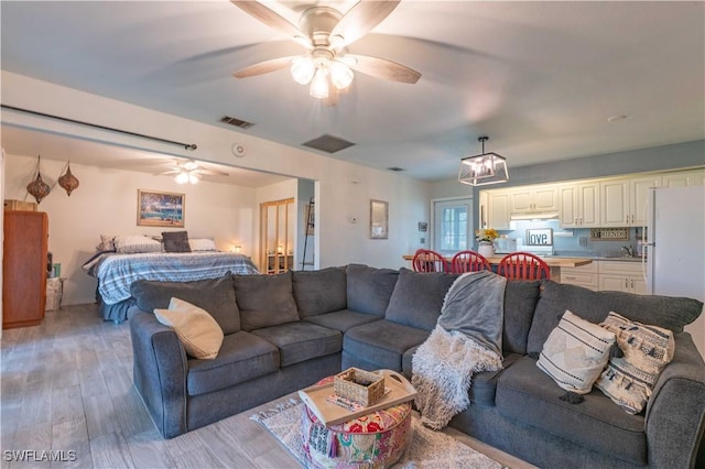 living room with a ceiling fan, visible vents, and light wood finished floors