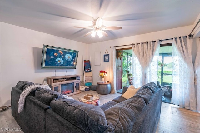 living area with a ceiling fan, wood finished floors, and a glass covered fireplace