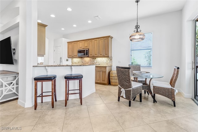 kitchen with stainless steel microwave, a kitchen bar, decorative backsplash, recessed lighting, and a sink