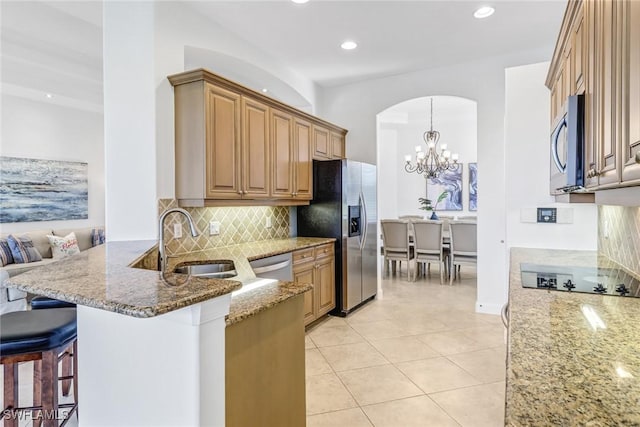 kitchen featuring light tile patterned floors, light stone counters, a sink, appliances with stainless steel finishes, and backsplash