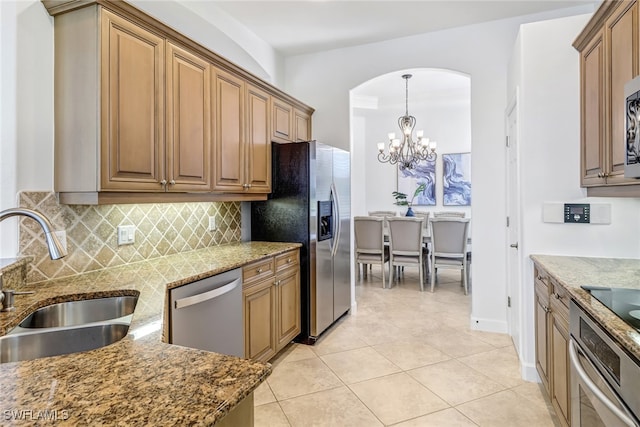 kitchen with light tile patterned flooring, stone countertops, a sink, appliances with stainless steel finishes, and tasteful backsplash