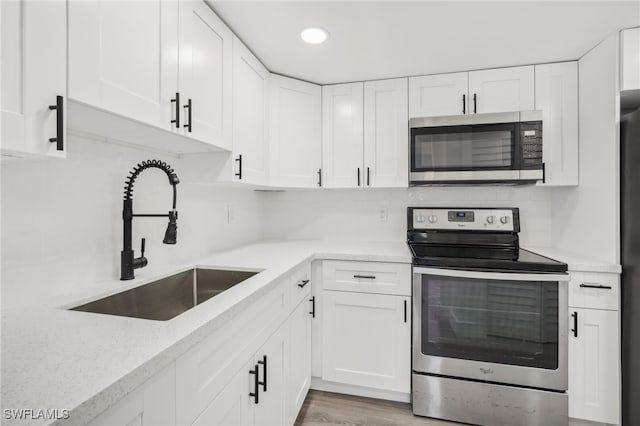 kitchen featuring white cabinets, light wood-type flooring, light stone countertops, stainless steel appliances, and sink