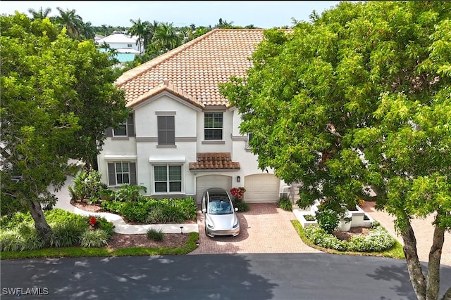 mediterranean / spanish home featuring a tiled roof, decorative driveway, an attached garage, and stucco siding