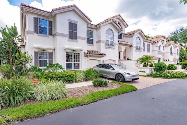 mediterranean / spanish-style house featuring a garage, decorative driveway, a tile roof, and stucco siding