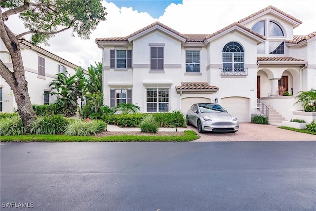 mediterranean / spanish-style house with a tiled roof, an attached garage, stairs, decorative driveway, and stucco siding