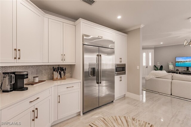 kitchen featuring crown molding, built in appliances, backsplash, and white cabinetry