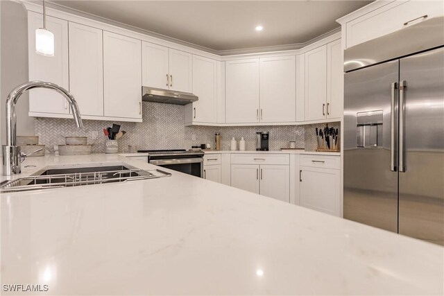 kitchen featuring pendant lighting, backsplash, stainless steel appliances, sink, and white cabinetry