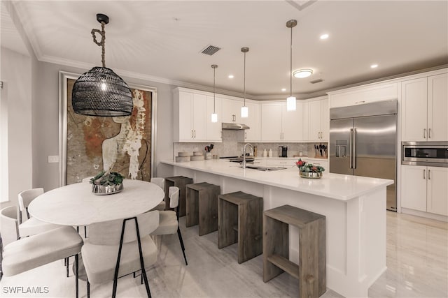 kitchen featuring white cabinetry, built in appliances, a kitchen breakfast bar, pendant lighting, and tasteful backsplash