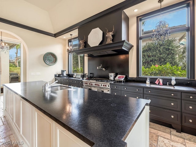 kitchen featuring sink, high end range, hanging light fixtures, a kitchen island with sink, and an inviting chandelier