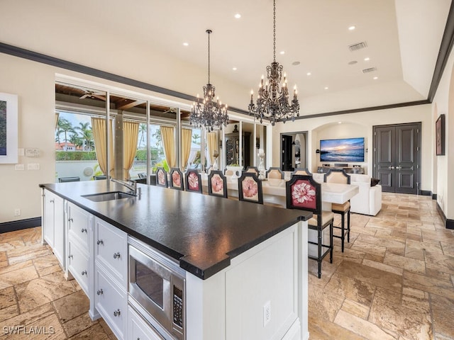 kitchen featuring sink, stainless steel microwave, pendant lighting, a kitchen island with sink, and white cabinets