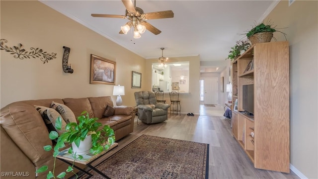living room featuring light wood-type flooring, a ceiling fan, baseboards, and ornamental molding