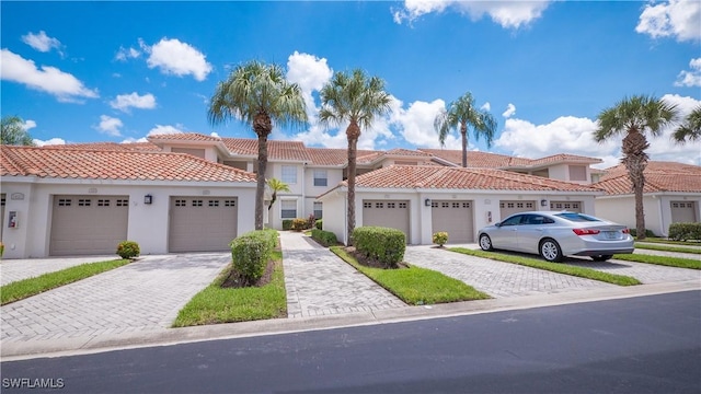 view of front of home with decorative driveway, stucco siding, a tile roof, and community garages