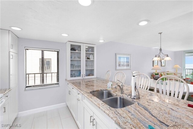 kitchen with pendant lighting, white cabinetry, sink, and light stone countertops