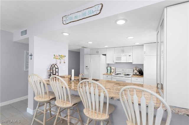 kitchen featuring white appliances, light stone counters, white cabinetry, sink, and a breakfast bar