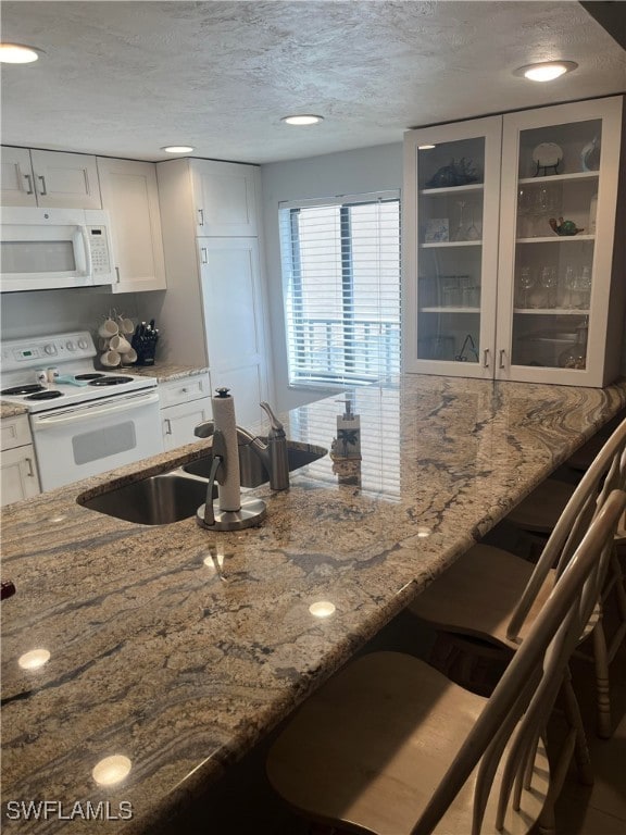 kitchen featuring white appliances, light stone countertops, white cabinets, and a textured ceiling